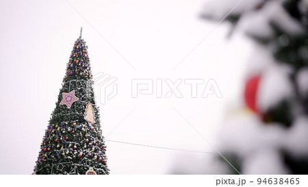 Background of the winter Christmas holiday - toys on a branch of a Christmas tree and blurry lights in the background in the background. Christmas tree in winter day. Christmas tree on the street, in 94638465
