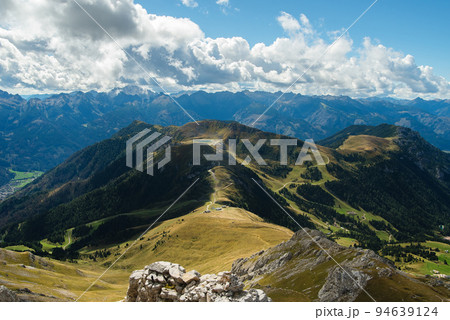 Sunny valley among majestic green cloudy mountain hills covered in green lush grass, and bushes. 94639124