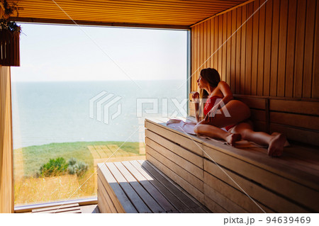 woman in a red swimsuit lies on a bench in the sauna with the panoramic window. woman in a red swimsuit lies on a bench in the sauna with the panoramic window. 94639469