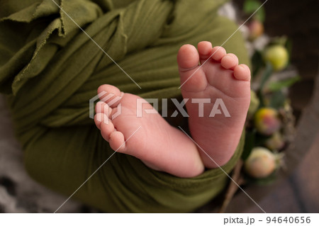 The tiny foot of a newborn. Soft feet of a newborn in a green woolen blanket. Close up of toes, heels and feet of a newborn baby. Studio Macro photography. Woman's happiness. 94640656