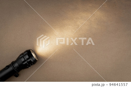 A bright beam of light from a flashlight shines on a brown recycled craft paper background. Old grunge vintage highly textured paper background 94641557