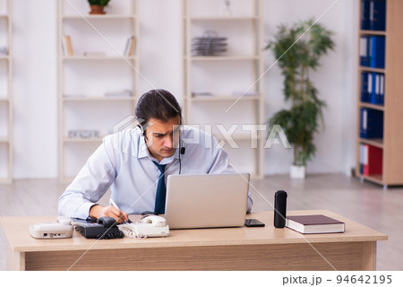 Young male call center operator working at his desk Young male call center operator working at his desk 94642195