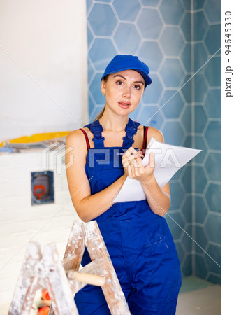 Focused woman dressed in work clothes checking quantity of tiles in documents during repair works Focused woman dressed in work clothes checking quantity of tiles in documents during repair works 94645330