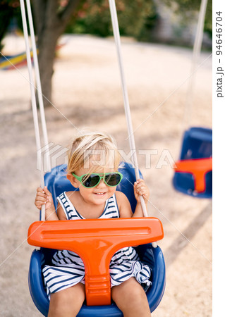 Smiling little girl in sunglasses swinging on a swing. High quality photo 94646704