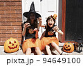 ハロウィンのコスチュームを着て装飾された家のドアの前にいる女の子2人 94649100