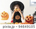 ハロウィンのコスチュームを着てみかんで作ったかぼちゃを持っている女の子 94649105