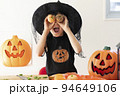 ハロウィンのコスチュームを着てみかんで作ったかぼちゃを持っている女の子 94649106