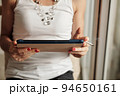 Hands of woman in white tank top smoking cigarette and reading e-book or article on tablet 94650161