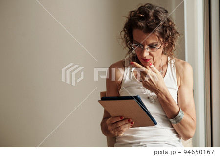 Shocked glam rock mature woman smoking when reading news article on tablet computer 94650167