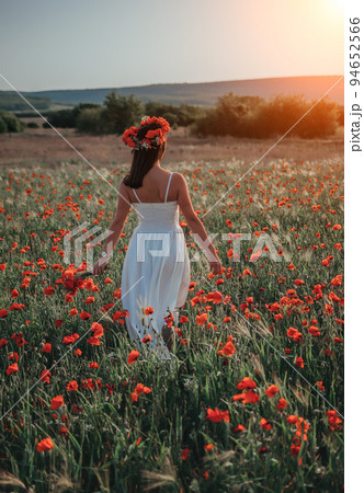 Bride in a white dress in a wreath of red poppies, warm sunset time on the background of the big red poppy field. Copy space. The concept of calmness, silence and unity with nature. Bride in a white dress in a wreath of red poppies, warm sunset time on the background of the big red poppy field. Copy space. The concept of calmness, silence and unity with nature. 94652566