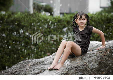 Cheerful child girl playing on heap of wet soil during raining in rainy season. 94653458