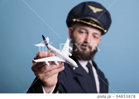 Airplane aviator in aircrew uniform looking at plane model, pilot playing with commercial passenger jet toy. Professional aviation academy aviator on blue background, medium shot Airplane aviator in aircrew uniform looking at plane model, pilot playing with commercial passenger jet toy. Professional aviation academy aviator on blue background, medium shot 94653878