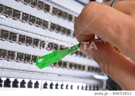 hand of administrator plugging in fiber optic cable into empty switchboard 94655652