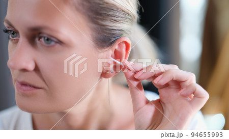 Closeup of young woman cleaning ear with cotton swab Closeup of young woman cleaning ear with cotton swab 94655993
