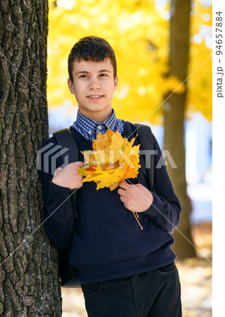 a teenage boy posing in autumn city park, trees with yellow leaves on a bright sunny day 94657884