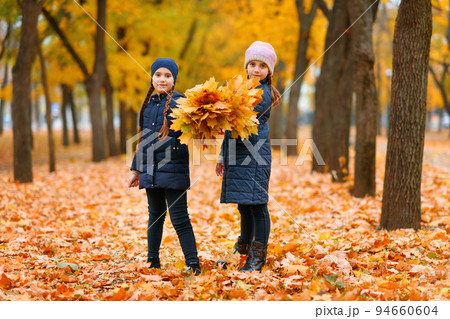 Girls playing and posing in autumn city park. Two children plays with yellow maple leaves. Fall season, beautiful nature with yellow trees. Girls playing and posing in autumn city park. Two children plays with yellow maple leaves. Fall season, beautiful nature with yellow trees. 94660604