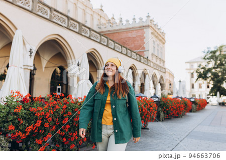 Young happy woman traveler in yellow hat listening to music through wireless earphones on urban background. Stylish female foreigner examines architectural monument during her long-awaited vacation Young happy woman traveler in yellow hat listening to music through wireless earphones on urban background. Stylish female foreigner examines architectural monument during her long-awaited vacation 94663706