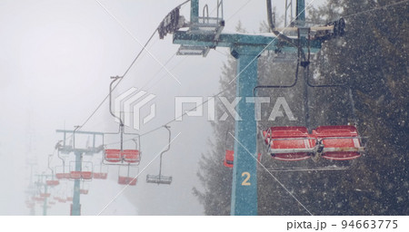 Empty ski lifts in snow winter, backdrop of mountain snowy forest. Ski chairlifts no motion. Stormy weather, snow blizzard in mountains ski resort without people. Nobody. Heavy snowfall 94663775