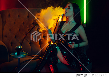 Sexy brunette model is smoking a hookah exhaling a smoke at a luxury night club. Sexy brunette model is smoking a hookah exhaling a smoke at a luxury night club. 94665778