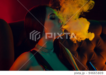 Sexy brunette model is smoking a hookah exhaling a smoke at a luxury night club. 94665809