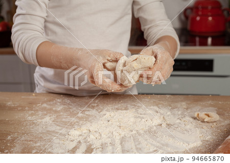 Beautiful little girl dressed in a white blouse is making a dough for baking a bread at a kitchen. Beautiful little girl dressed in a white blouse is making a dough for baking a bread at a kitchen. 94665870