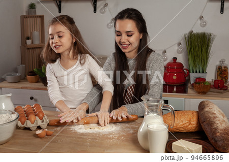 Mother and her daughter are baking a bread and having fun at the kitchen. 94665896