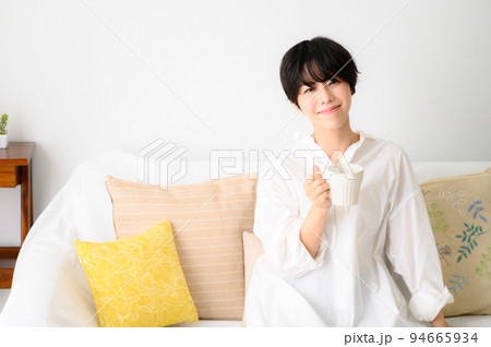 部屋でくつろいでコーヒーなどの飲み物を飲む女性 94665934