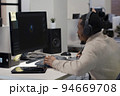 African American designer in headphones draws on tablet 3D models for games. 94669708