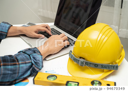 Asian engineer with architectural house plan project blueprint, graph and yellow helmet and engineering construction tools. 94670349