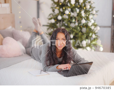 woman in cozy grey knitted sweater using laptop on bed , xmas holiday woman in cozy grey knitted sweater using laptop on bed , xmas holiday 94670385