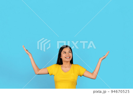 Surprised glad inspired young japanese lady in yellow t-shirt raises hands up, holds empty space Surprised glad inspired young japanese lady in yellow t-shirt raises hands up, holds empty space 94670525