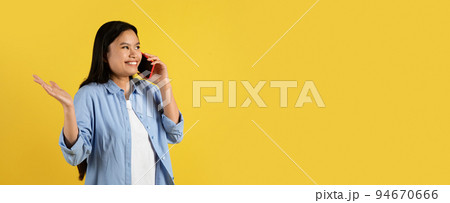 Cheerful confused excited young chinese female student in casual gesturing and calling on smartphone 94670666