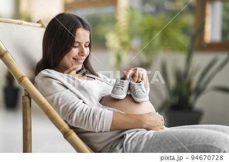 Maternity Concept. Pregnant Beautiful Woman Holding Small Baby Shoes Near Her Pregnant Belly And Smiling Maternity Concept. Pregnant Beautiful Woman Holding Small Baby Shoes Near Her Pregnant Belly And Smiling 94670728