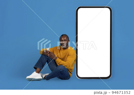 Cheerful african american man sitting on floor, using cell phone Cheerful african american man sitting on floor, using cell phone 94671352