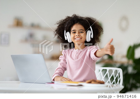 Black girl schooler using laptop and headphones, showing thumb up 94671416