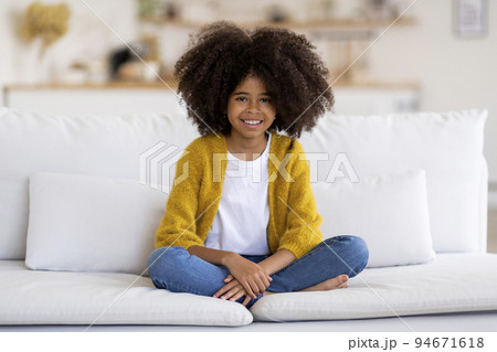 Cheerful african american girl sitting on couch at home Cheerful african american girl sitting on couch at home 94671618