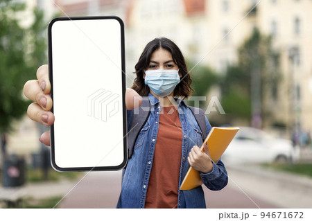 Young Arab Woman In Medical Mask Showing Blank Smartphone While Standing Outdoors Young Arab Woman In Medical Mask Showing Blank Smartphone While Standing Outdoors 94671672