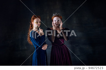 Portrait of two beautiful women in image of queens in face masks over dark background. Skincare 94672523