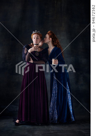 Portrait of two beautiful women in image of queens isolated over dark background. Whispering secrets and gossips 94672562