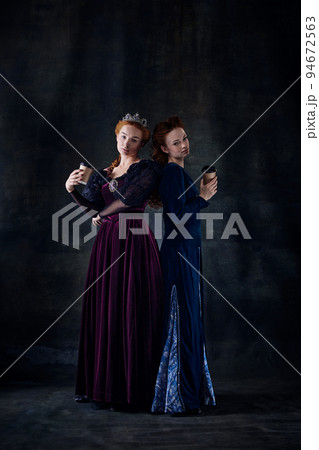 Portrait of two beautiful women in image of queens isolated over dark background. Coffee break 94672563