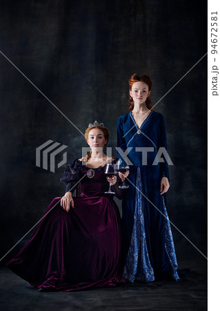 Portrait of two beautiful women in image of queens isolated over dark background. Royal family legacy 94672581