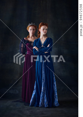 Portrait of two beautiful women in image of queens isolated over dark background. Royal family portrait 94672598