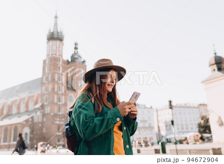 Beautiful stylish woman in hat walking on Market Square in Krakow on autumn day and holding mobile phone. Phone Communication. Urban lifestyle concept. Check social networks, send sms. Beautiful stylish woman in hat walking on Market Square in Krakow on autumn day and holding mobile phone. Phone Communication. Urban lifestyle concept. Check social networks, send sms. 94672904