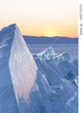 Winter landscape with ice hummocks glittering in the sun and mountains of Lake Baikal in Siberia at sunset. Natural background. 94673507
