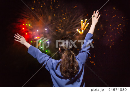 A young brunette woman enjoys the fireworks in the sky.Concept of festivals and holidays with fireworks. The view from the back 94674080