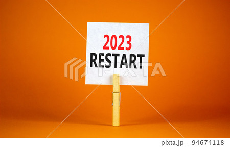 2023 Restart symbol. White paper with words 2023 Restart, clip on wooden clothespin. Beautiful orange table orange background. Business and 2023 restart concept. Copy space. 2023 Restart symbol. White paper with words 2023 Restart, clip on wooden clothespin. Beautiful orange table orange background. Business and 2023 restart concept. Copy space. 94674118