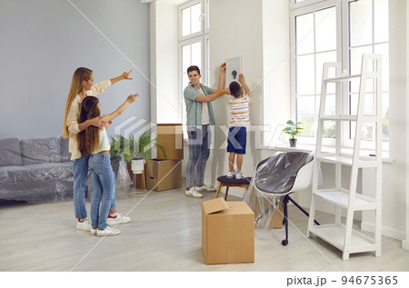 Happy family are hanging picture on wall while decorating their newly bought house Happy family are hanging picture on wall while decorating their newly bought house 94675365