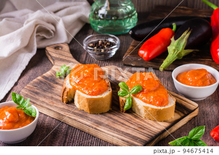 Spicy appetizer ajvar on pieces of bread and in bowls on the table 94675414