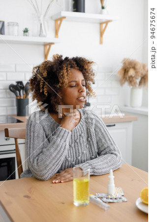 African American woman with a cold and sore throat drinks vitamins and measures body temperature. African American woman with a cold and sore throat drinks vitamins and measures body temperature. 94675674