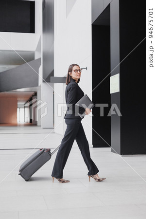 business tourism, business woman in a formal suit with a smartphone in a business center or airport with a suitcase goes on a business trip 94675701